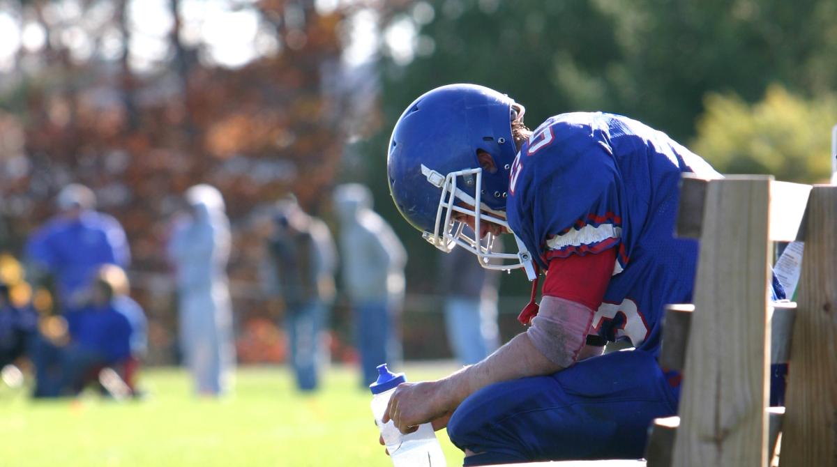 — title missing — Football player resting on bench with head down