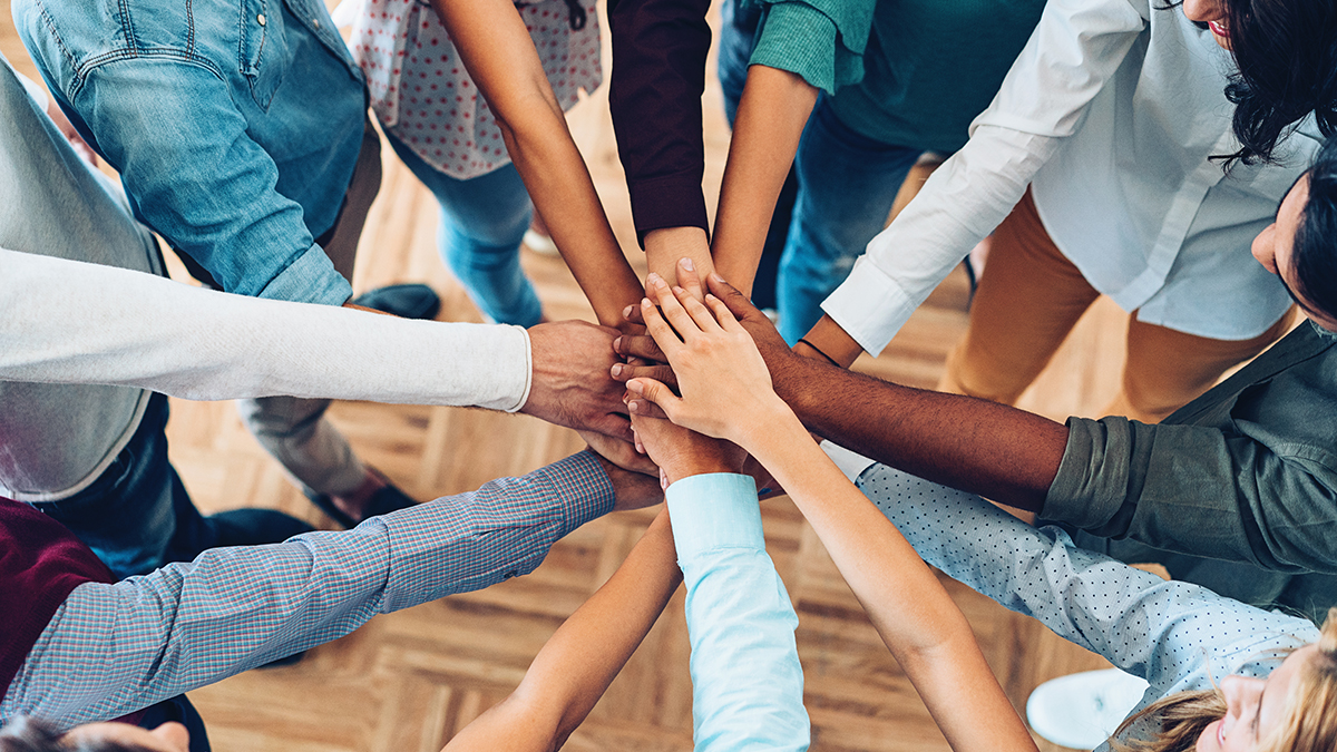 — title missing — Multi-ethnic group of people standing in a circle with their hands in the center.