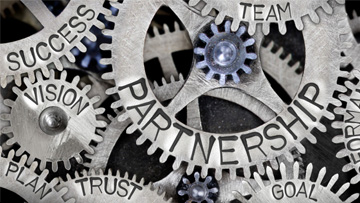 — title missing — Photo of tooth wheel mechanism with Partnership related words imprinted on metal surface