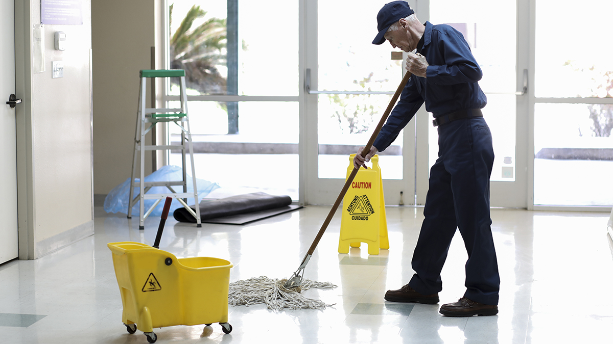 — title missing — Senior adult janitor mops floors at entry to offices.