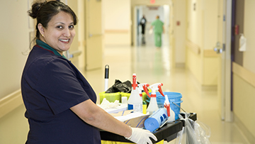 — title missing — Adult cleaner with cleaning cart in a hospital hallway.