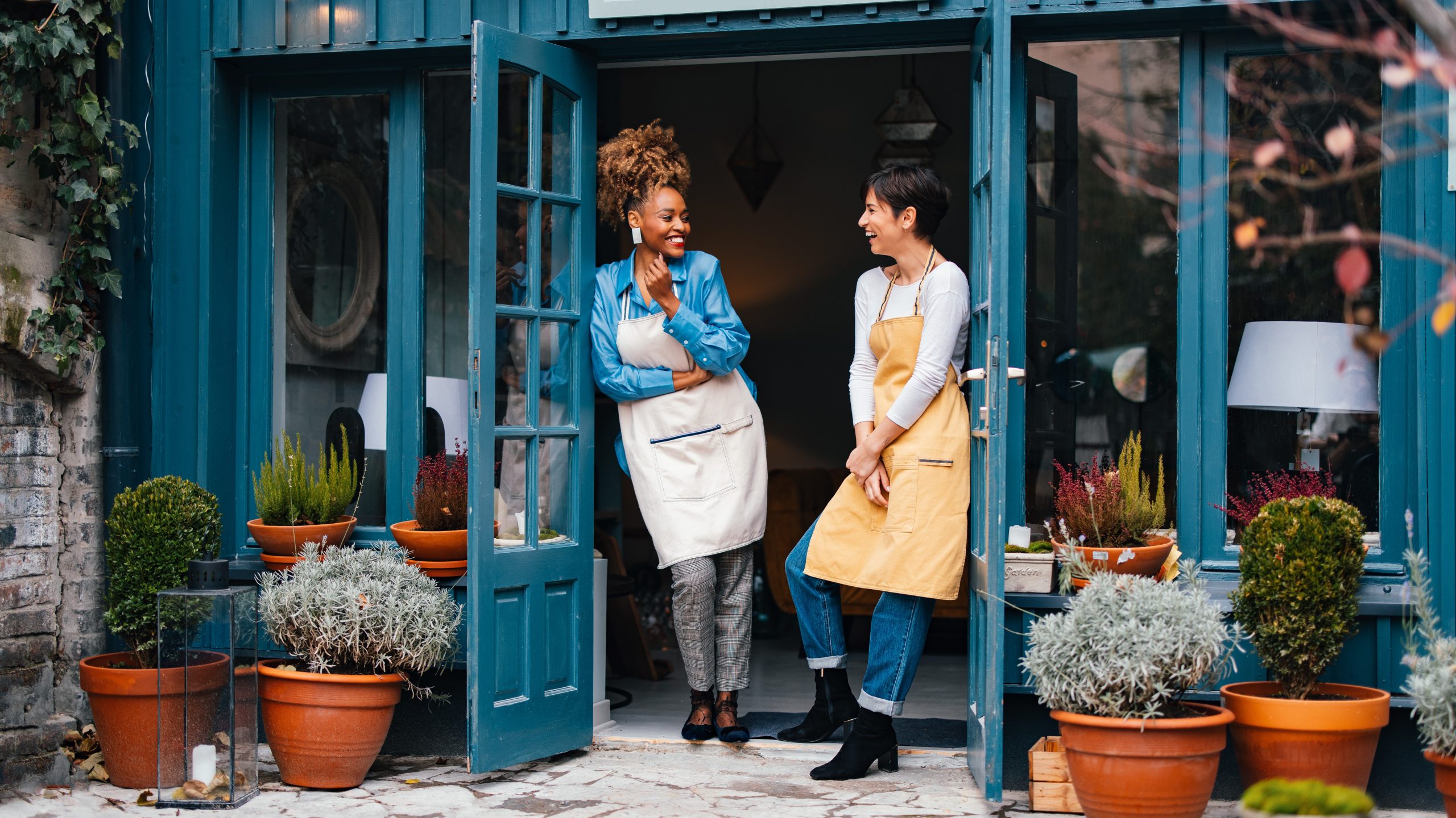 SBA Banner & Thumbnail Happy African-American woman and her employee talking and laughing while standing at door of the store.