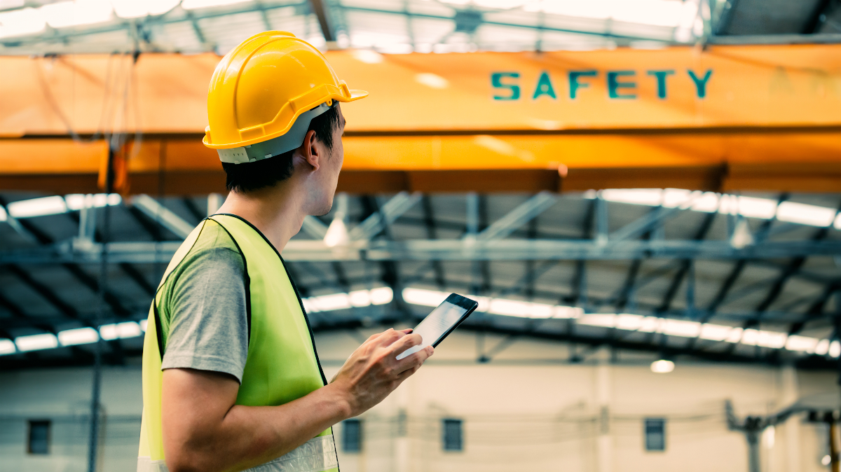 — title missing — Man with hard hat and safety vest walking under a sign that says safety