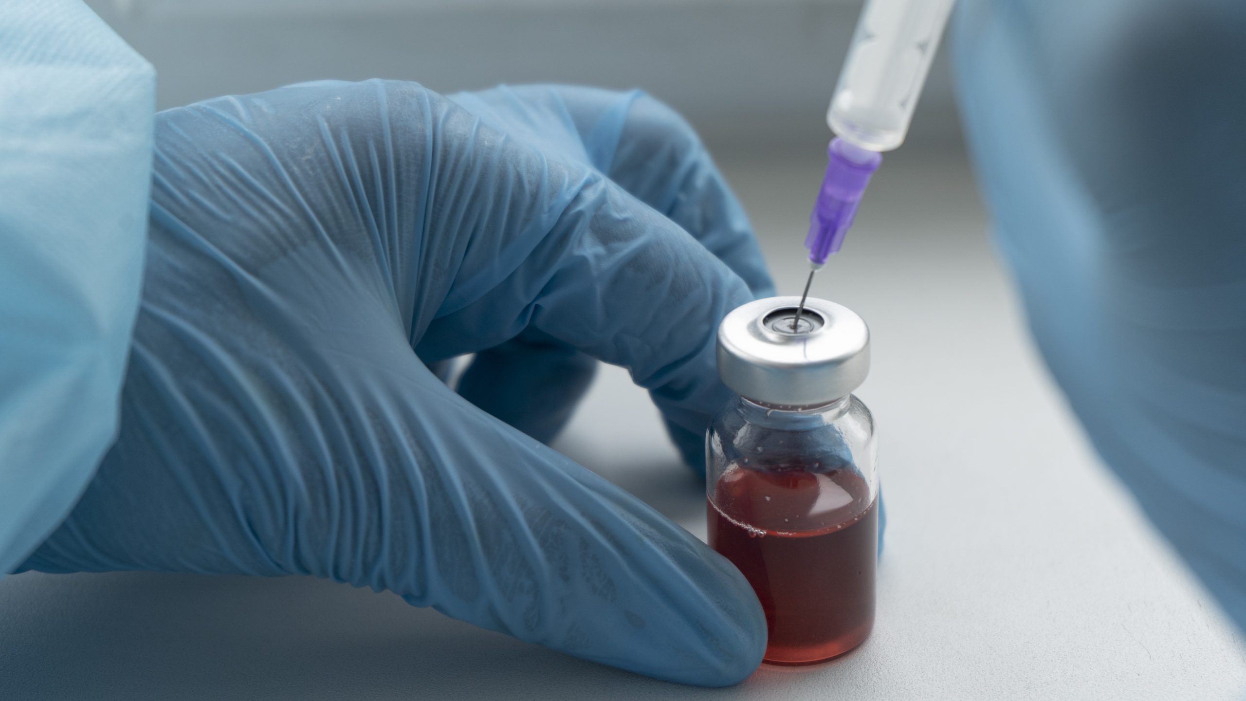 -- title missing -- A healthcare worker in a protective suit and gloves inserting a needle into a vial.