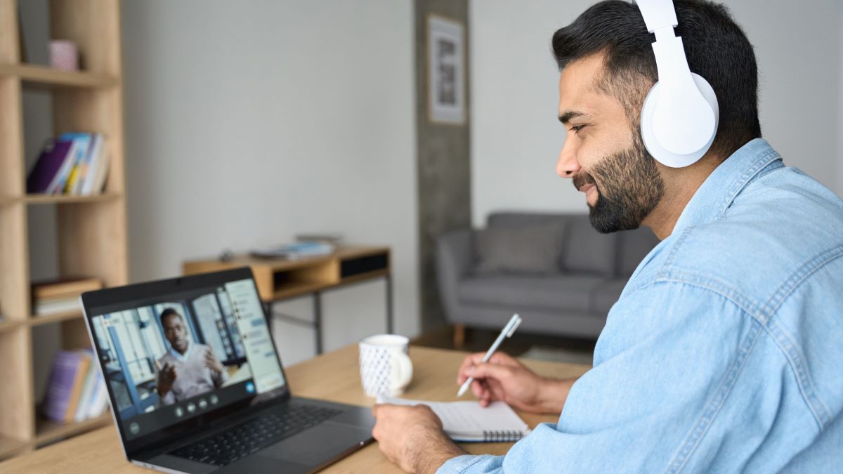 Work flexibility Man with dark hair and a beard, wearing large headphones, is participating in a virtual meeting on his laptop.