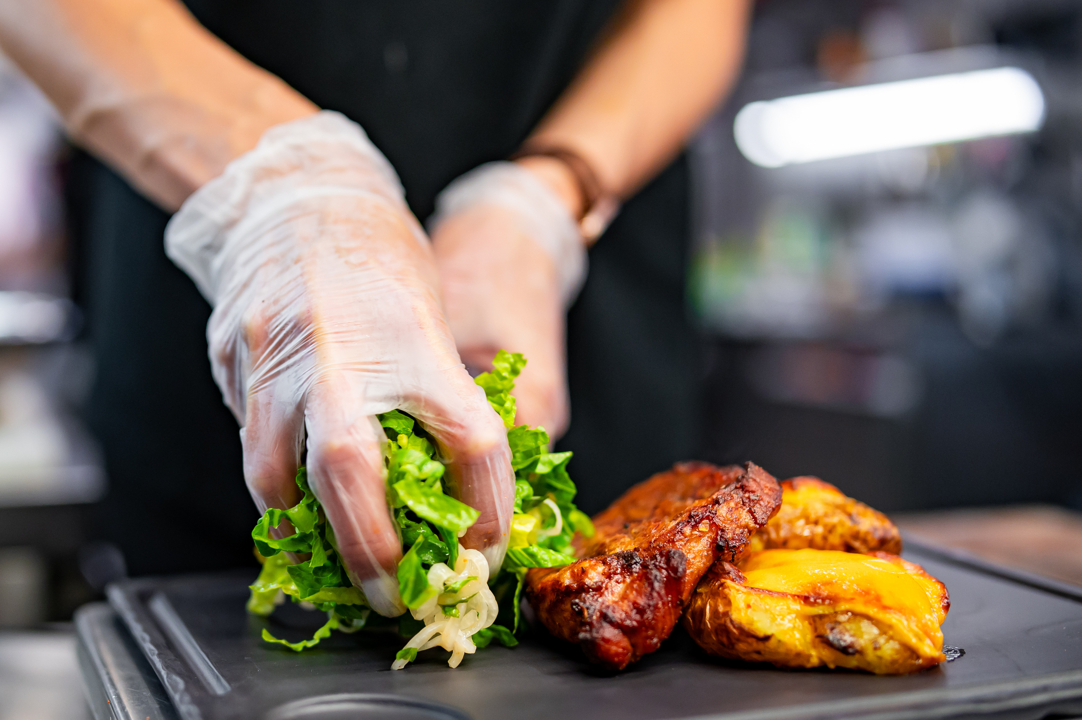 food prepared at restaurant Restaurant chef with gloved hands placing salad and meat on plate.