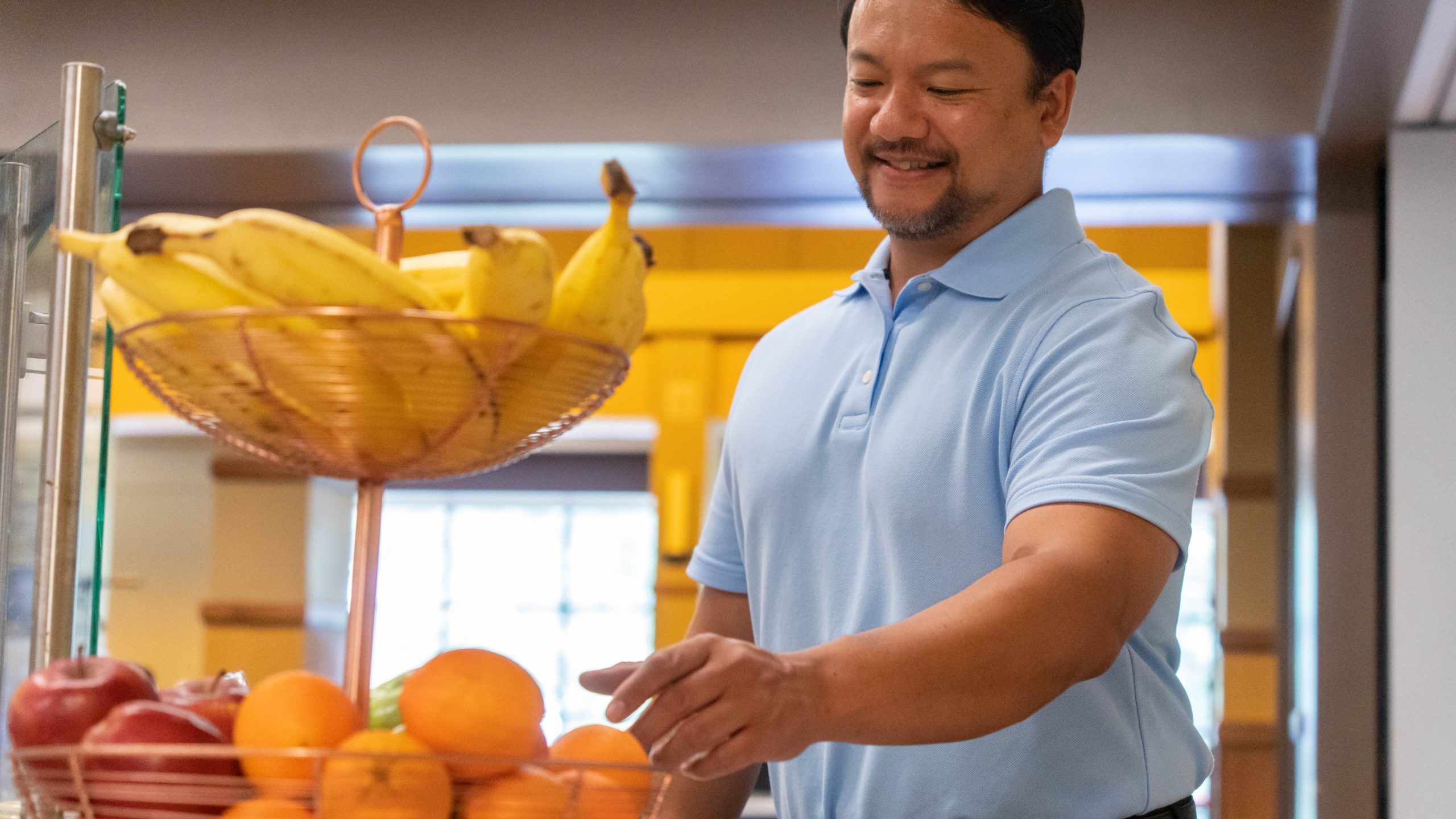— title missing — Man reaches for an orange in a display of bananas, apples, and oranges.