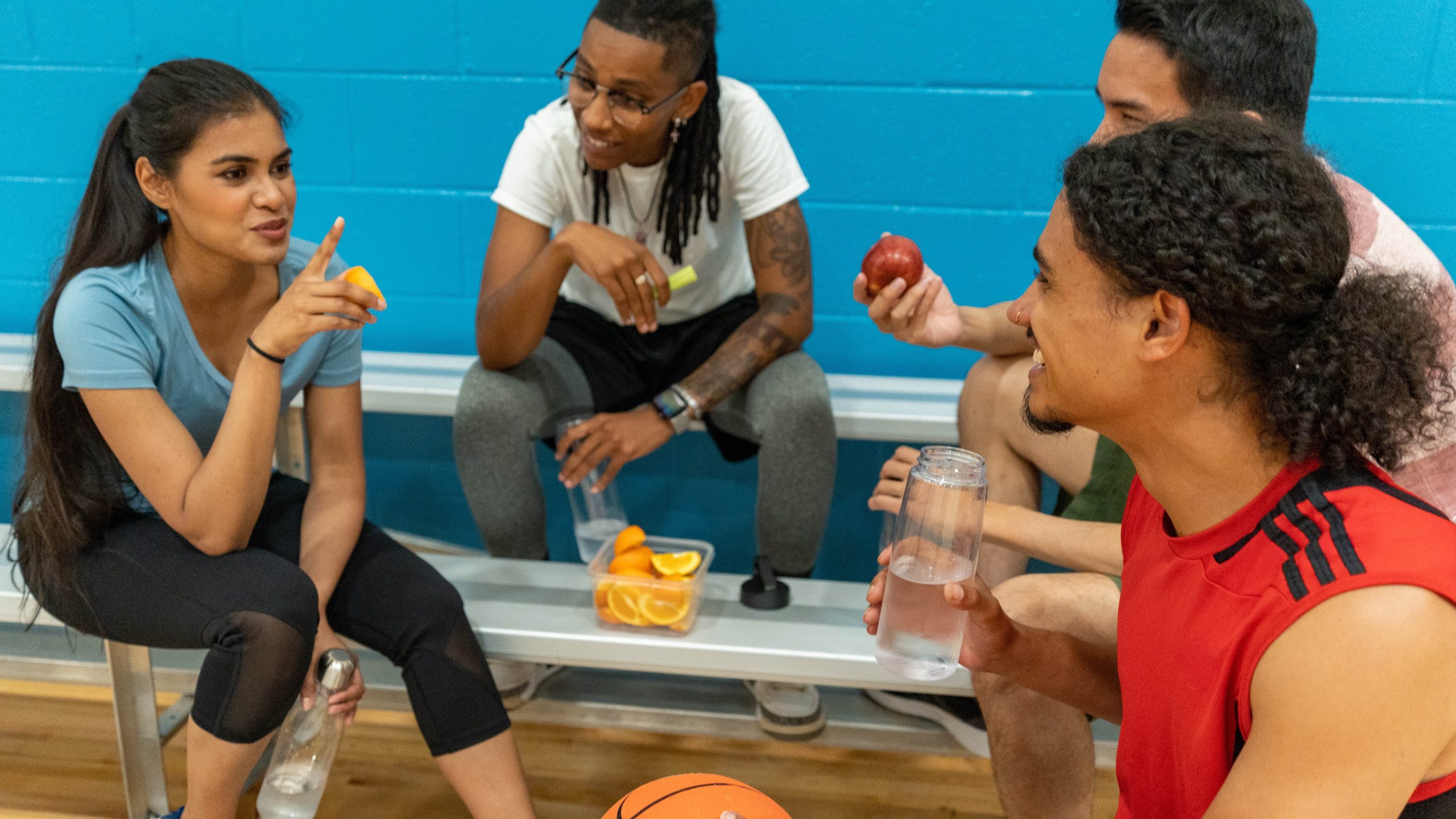 Basketballwithhealthysnacks169.jpg Four young people eating healthy snacks while taking a break from playing basketball.
