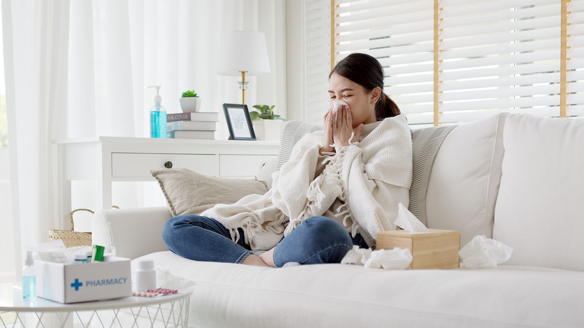 Girl blowing nose Sick young Asian teen sitting under the blanket on sofa and sneeze with tissue paper at home