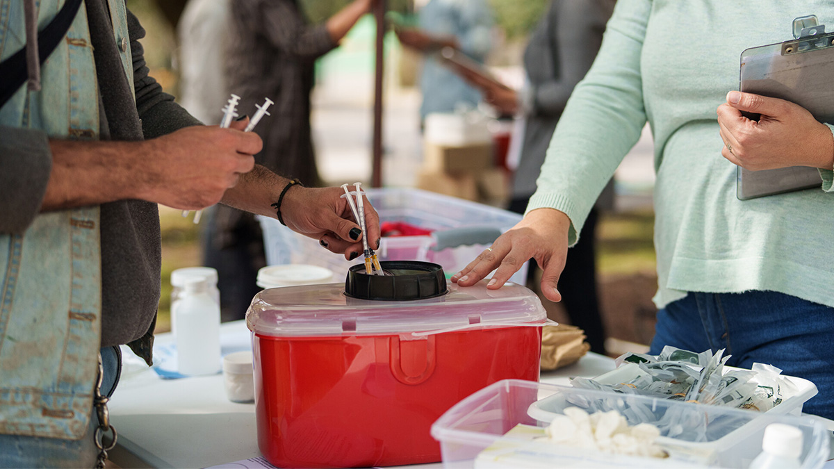 Man disposes needles at SSP A man deposits used syringes into a red disposal container.