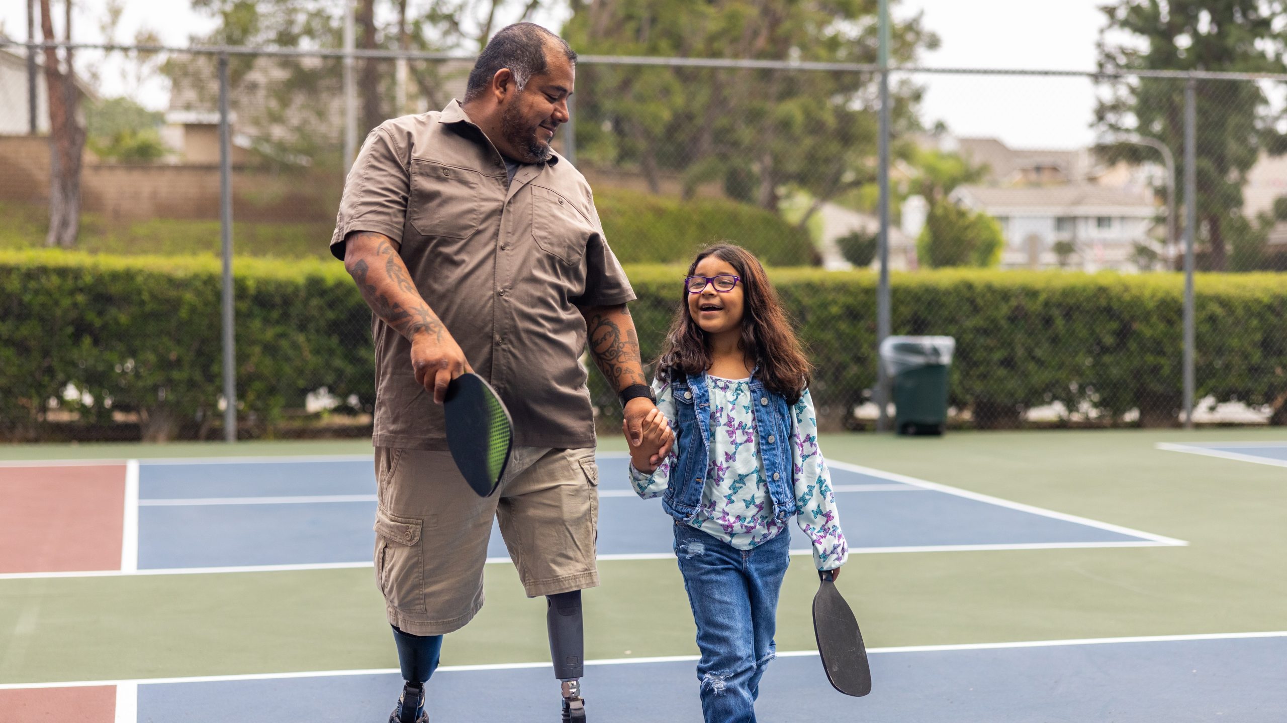 — title missing — Father with prosthetic legs and daughter on pickleball court.
