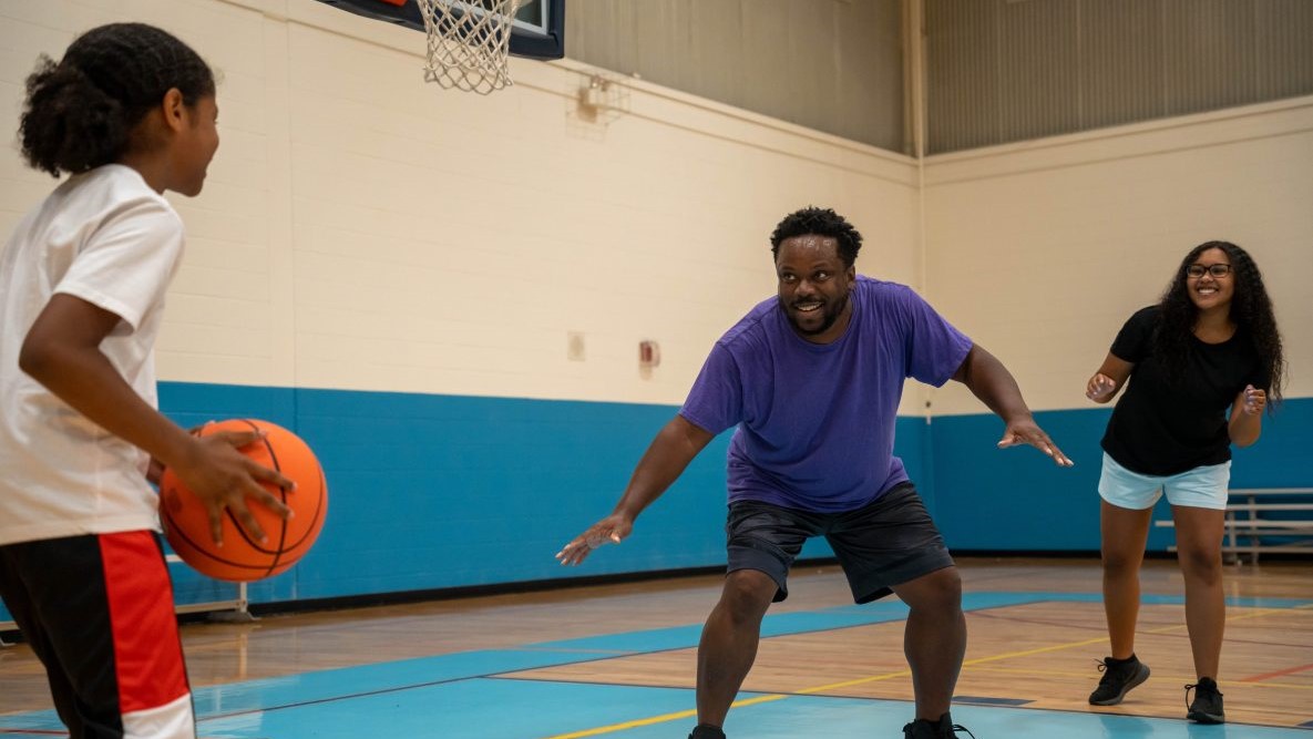 -- title missing -- Father inside a gym playing basketball with two children.