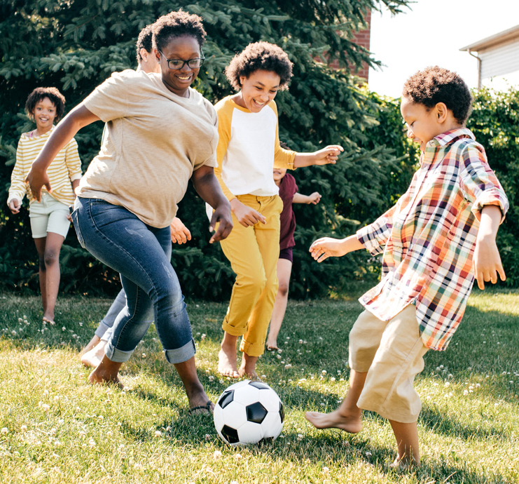 Creating childhood memories Adult woman playing soccer with children.