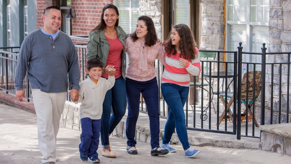 LatFamilyWalking169.jpg Family of five walking on sidewalk in front of houses.