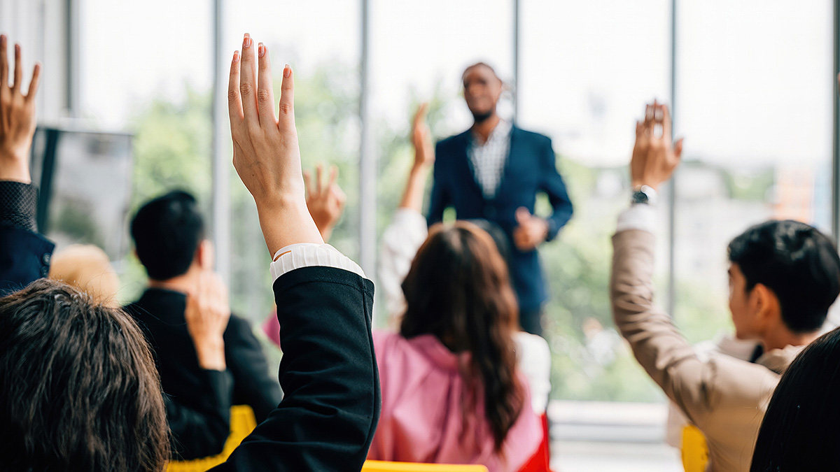 PLACES Asking Questions African-American speaker in background with many people in audience with hands raised with questions