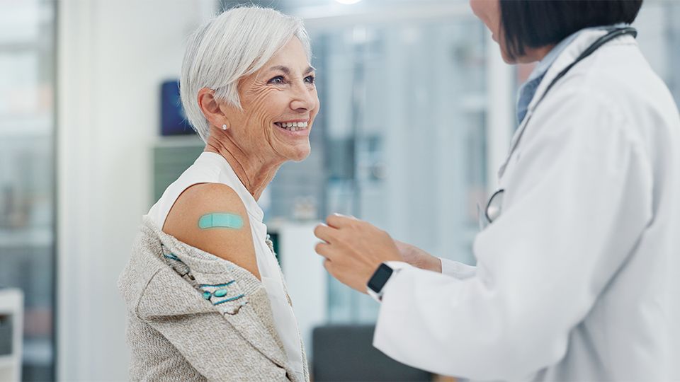 older adult at doctor's with bandaid Doctor putting a blue bandaid on older adult woman's arm.