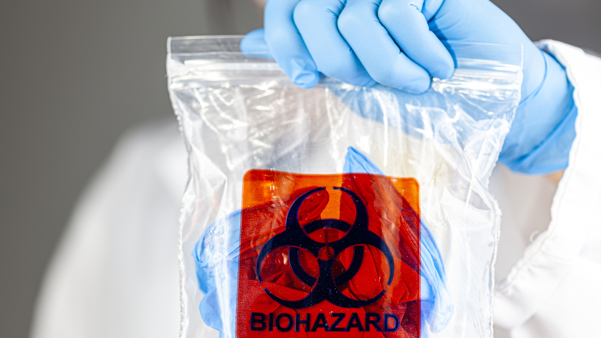gloved hand of laboratory worker holding up a hazardous waste bag