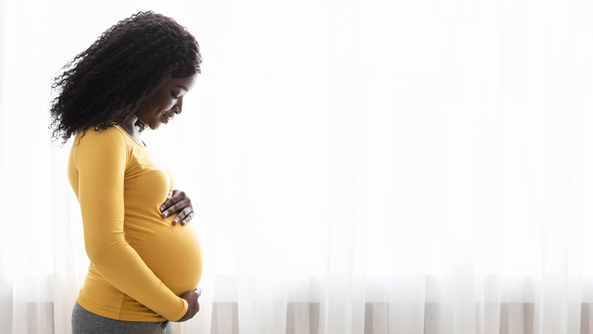 Joyful and Determined Pregnant Woman A woman in a yellow shirt holds her pregnant belly.