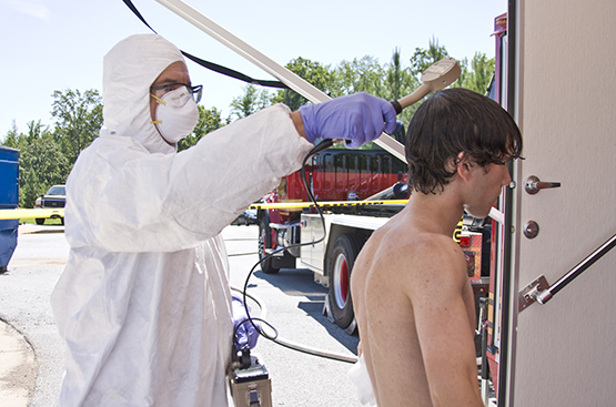 — title missing — A young man being washed at a decontamination station by a suited health worker.