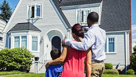Radon new home 456px A family with their backs turned stands in front of a house on a sunny day.