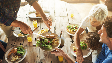 CDC food image Two people sitting at a wooden table being served food by another person who is standing.