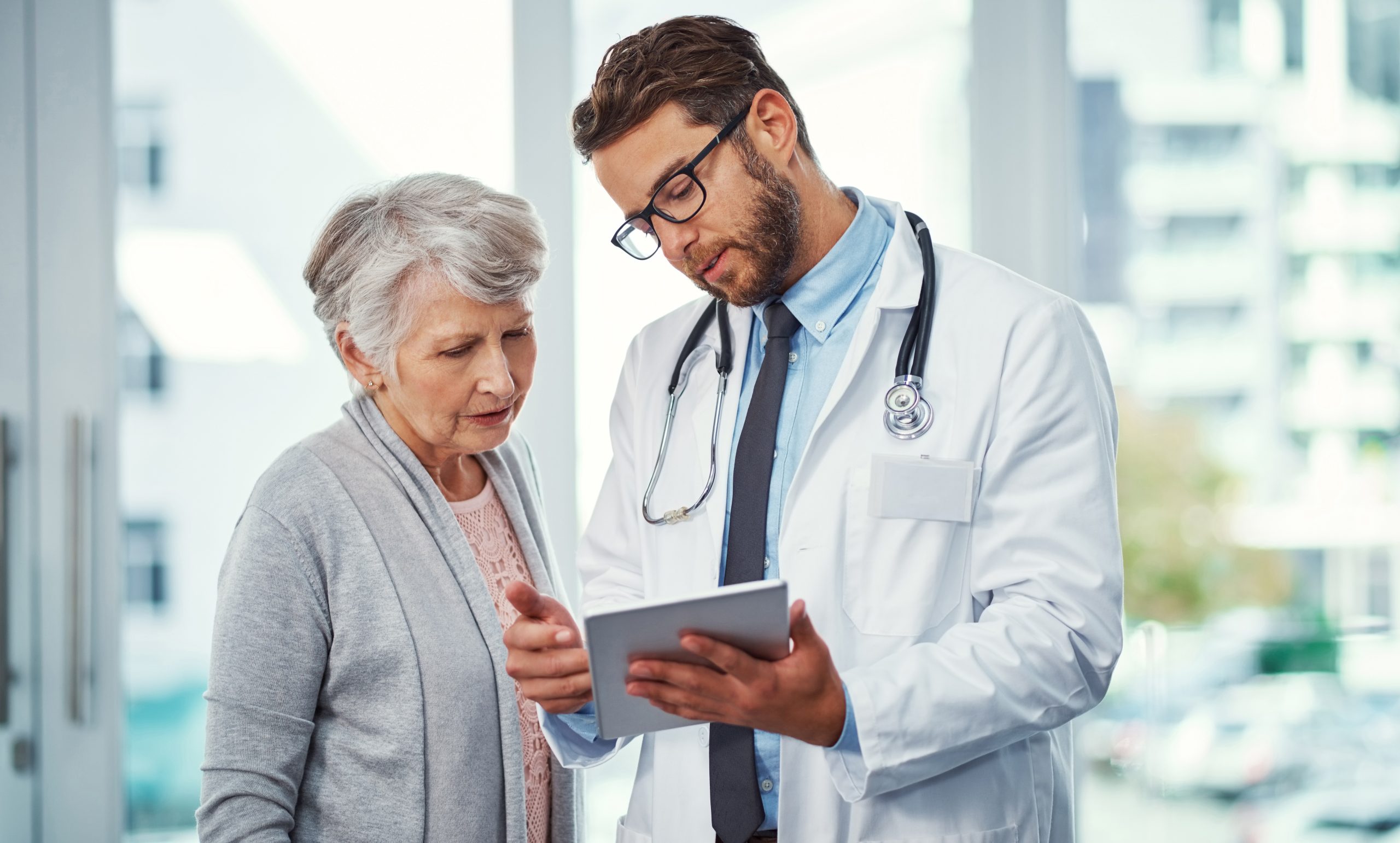 Clinical Overview A doctor holding a clipboard speaking to an older patient. Both doctor and patient are looking at the clipboard.