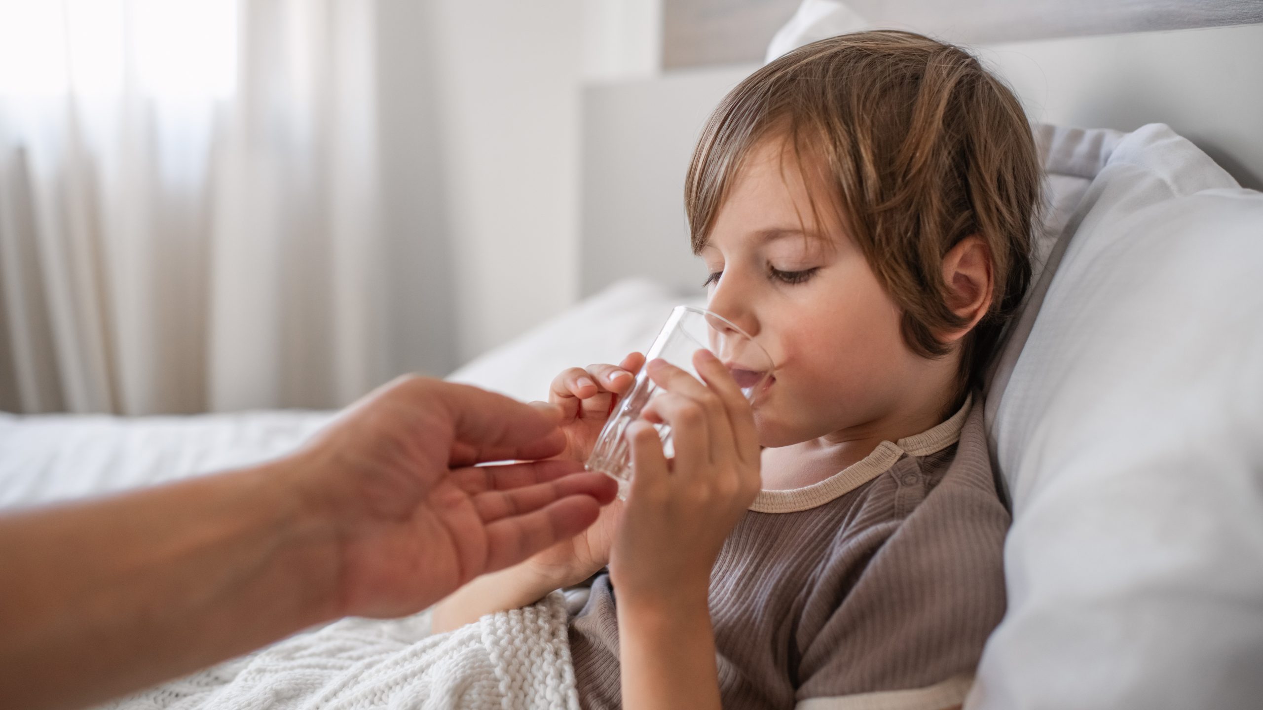 Salmonella - Treatment - Child Drinking Water A child propped up in bed drinking water. The glass is being supported by a man's hand.