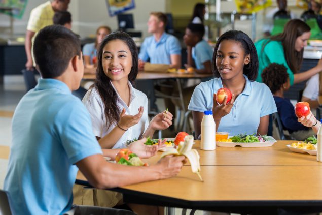 Students eating lunch Three students eating lunch at a table together in a school cafeteria.