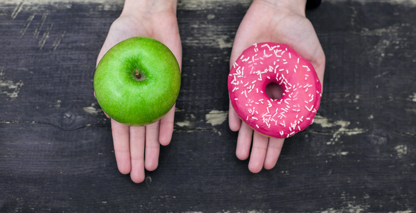 Donut or Apple Two open hands. One hand is holding a green apple. The other hand is holding a pink donut with sprinkles.