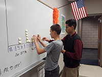 kristen-endle Two diverse students engage in a lesson on a whiteboard in a classroom setting.