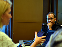 kurt-jones A man listens to a woman speaking at a table filled with laptops.
