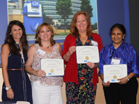 sumi-jayaraman A diverse group of four women standing in front of a projected graphic holding certificates.