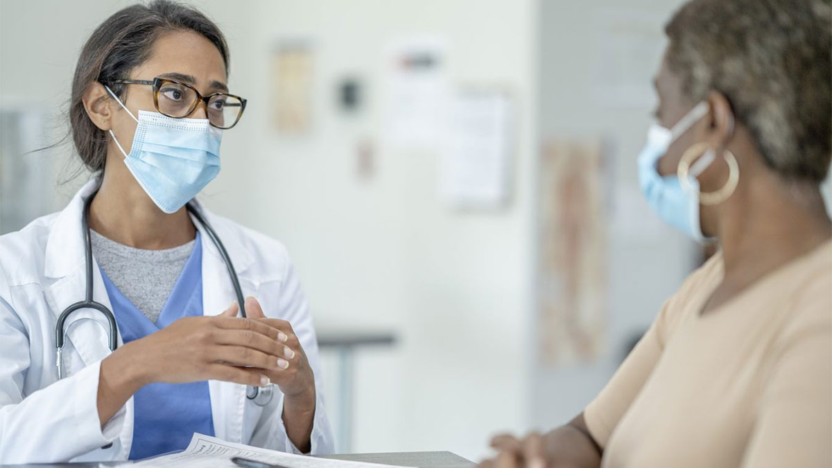 doctor-patient-social-twitter A doctor in a mask talks to an older female patient in a mask.