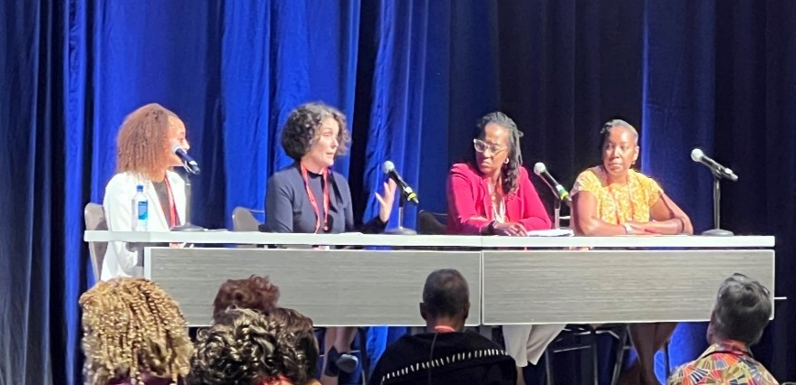 SCDAA panel Four persons sit at a table with microphones on a stage
