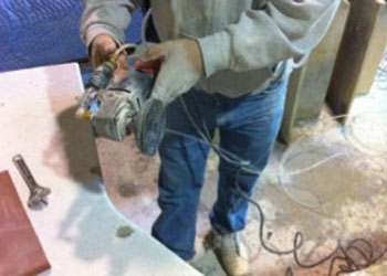 2015-106-grinder Un trabajador usa una amoladora angular con un disco de pulido para hacer el acabado de un mesón de piedra. La herramienta con toma de agua ayuda a reducir la exposición al polvo de sílice cristalina respirable que se genera durante las operaciones de amolado y pulido.