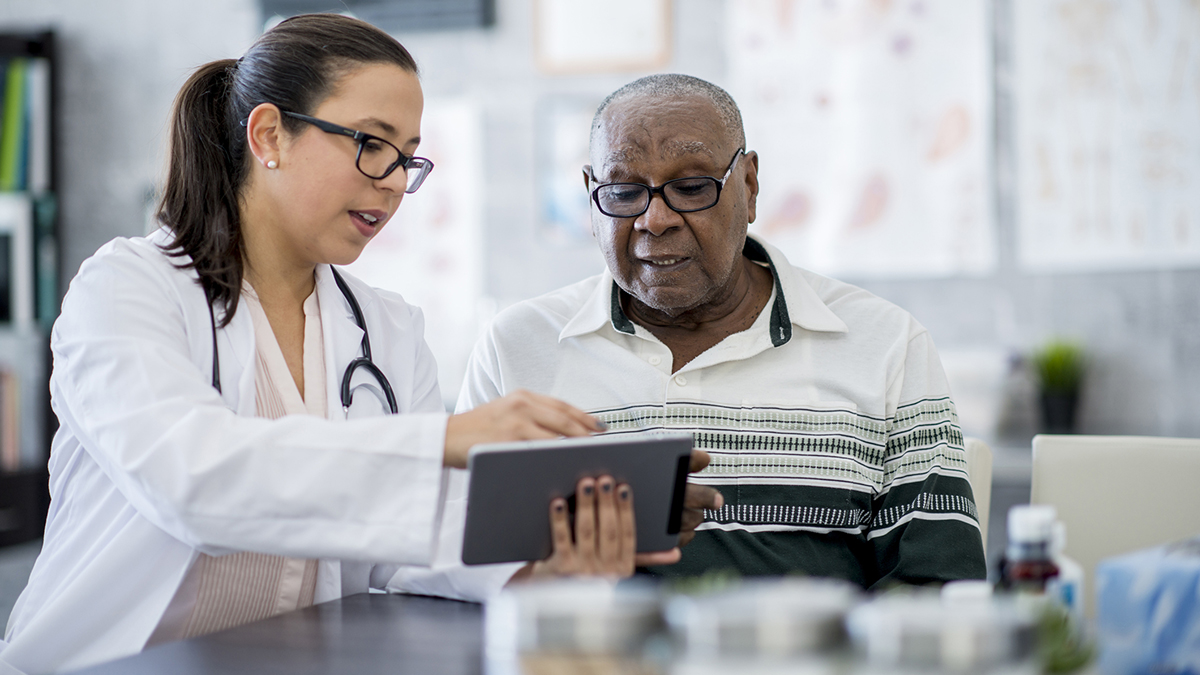 Doctor With A Tablet Computer White female doctor with brown hair in a low ponytail with Black older adult patient looking at a tablet.