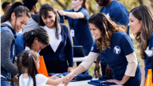 community-event a woman surrounded by other women volunteering at a table and shaking hands with a little girl