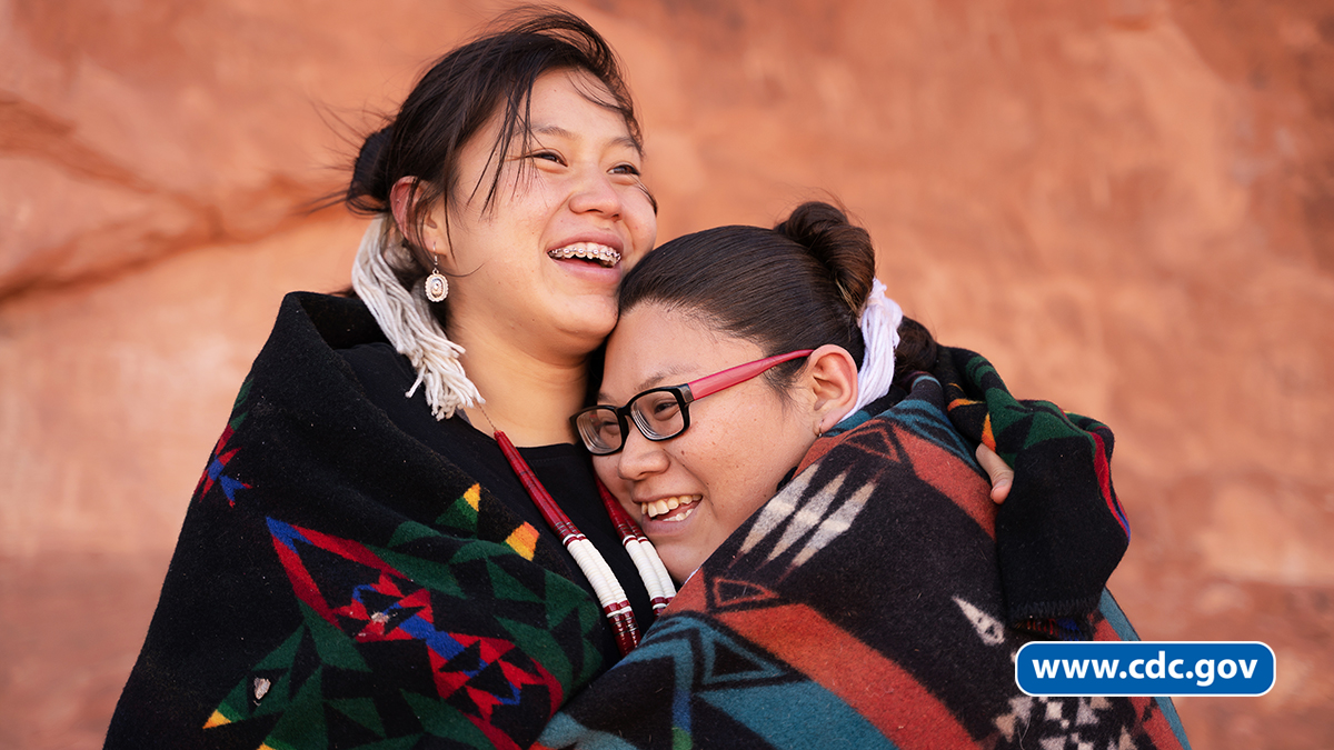 -- title missing -- Two Native American/Alaska Native women hugging and smiling.