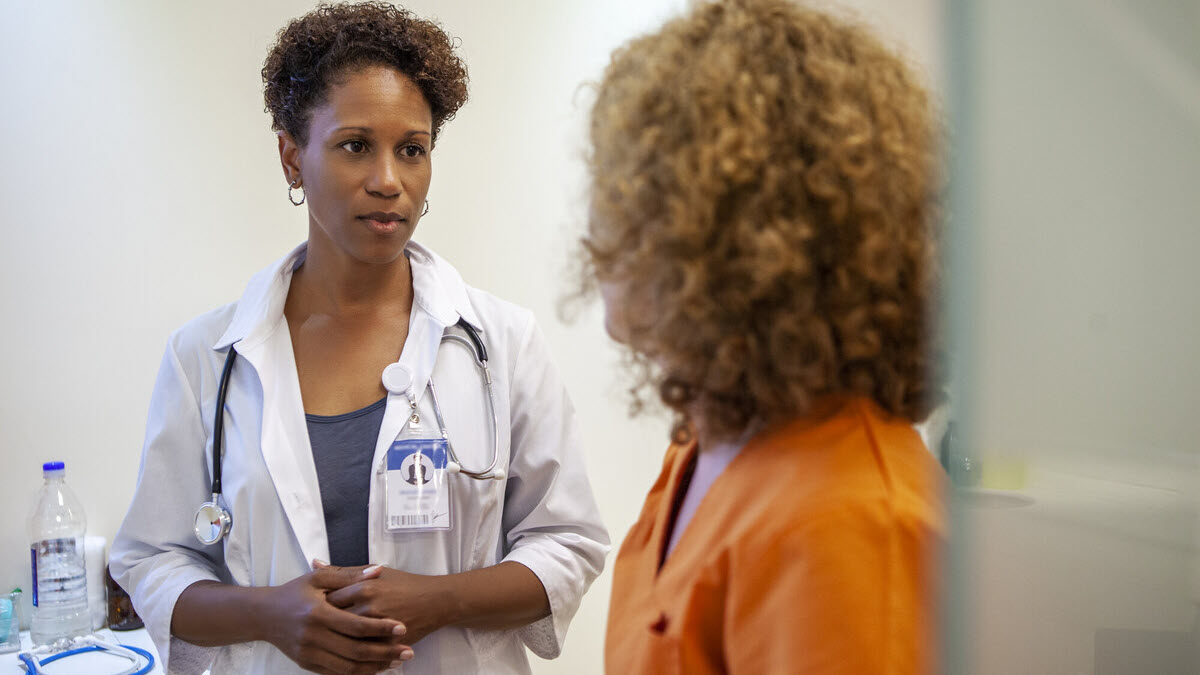 Doctor and patient correctional facility Mid shot of African-American female doctor talking to incarcerated woman wearing orange jumpsuit in correctional healthcare facility