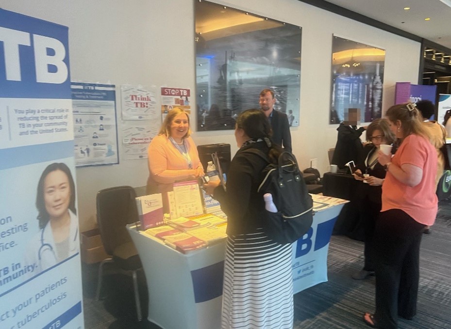 National TB Conference Exhibit CDC employee standing behind exhibit booth talking to members at the National TB Conference