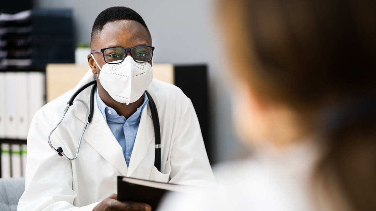 Health care provider wearing respirator A male health care provider wearing a respiratory speaks to a female patient.