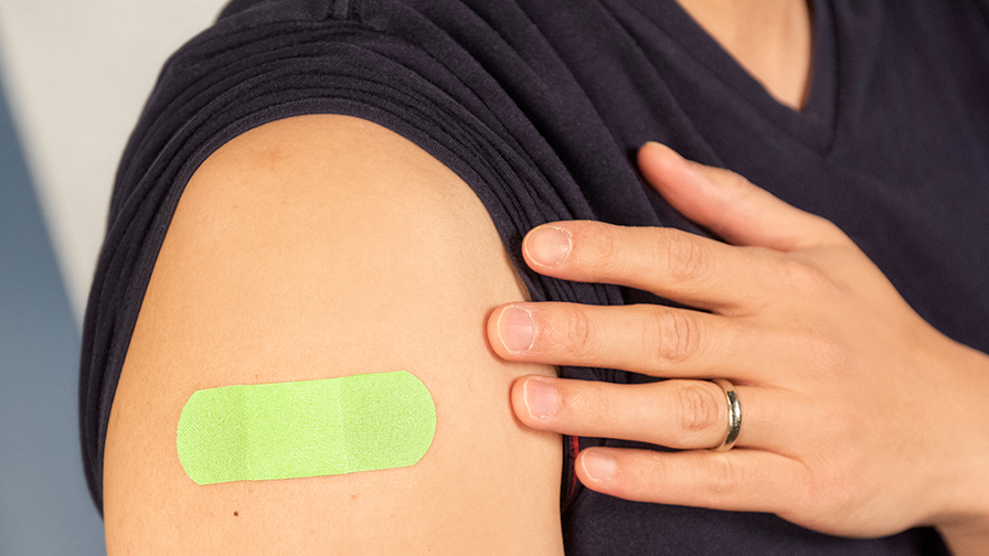 bandaid after vaccination Person shows green bandage on arm after vaccination.
