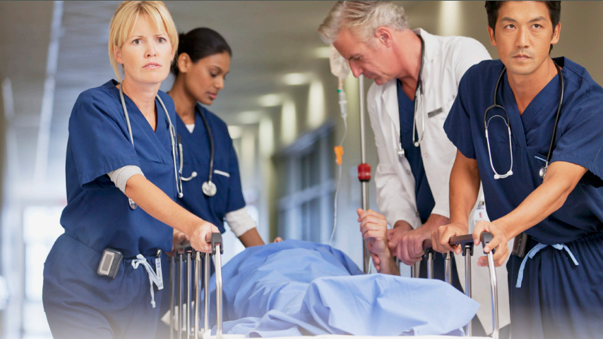 Clinicians in hospital Clinicians pushing a hospital bed with a patient lying on it.