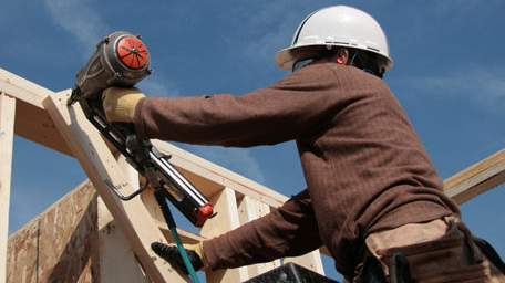 — title missing — A construction worker uses a nail gun to build a house.