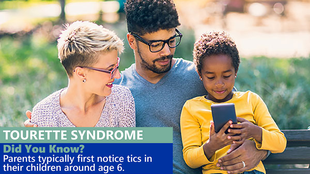 tourette-syndrome-did-you-know-1200px-675px Parents sit on park bench with their daughter, looking and smiling at a cell phone.