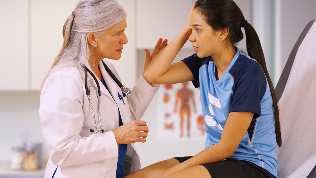 — title missing — Doctor talks with young patient gesturing towards her head