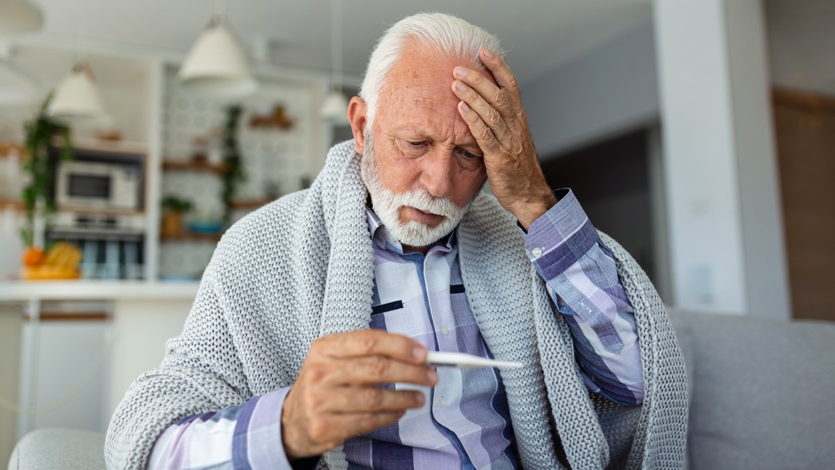 Older man with headache and thermometer An older man with a headache holds a thermometer.