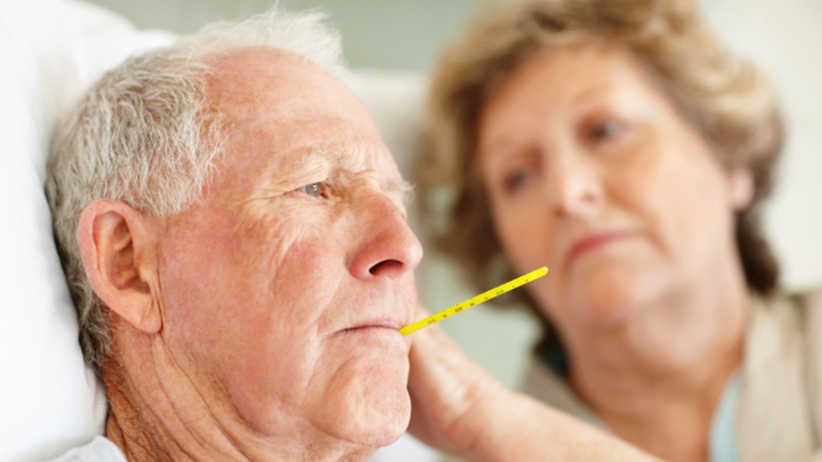 Worried senior woman comforting a sick elderly man Person sick in bed with thermometer.