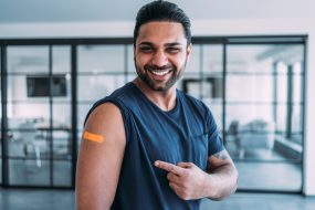 Reasons vaccinate 3 An adult man smiling and pointing to his arm after getting his shot.