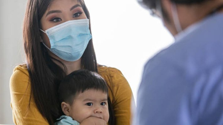 Mom holding child at doctor's office Masked mom holds her child in front of a doctor at an appointment.
